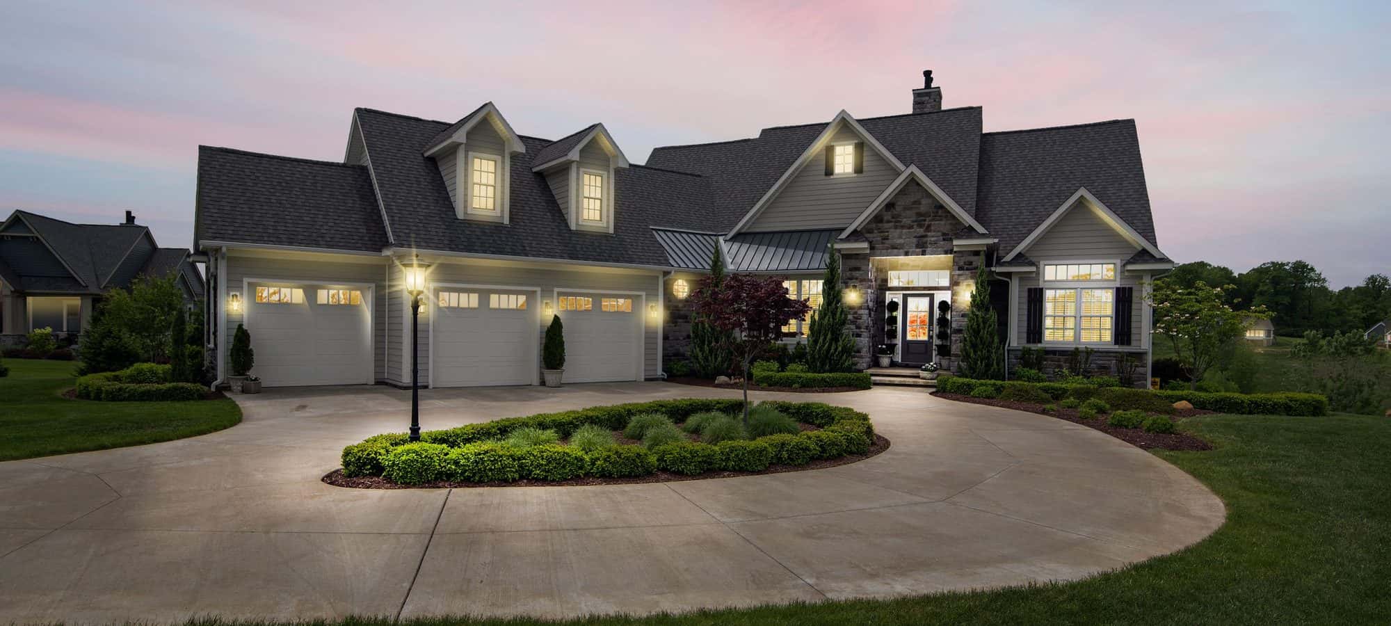 Modern suburban home at dusk with landscape lighting along the driveway and facade