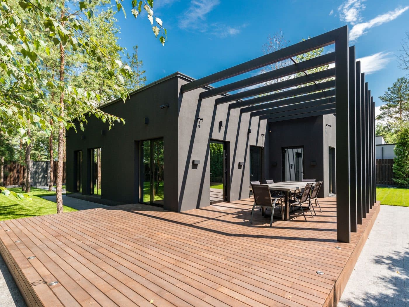 Wooden deck with a dining set framed by mature shrubs and a shade tree