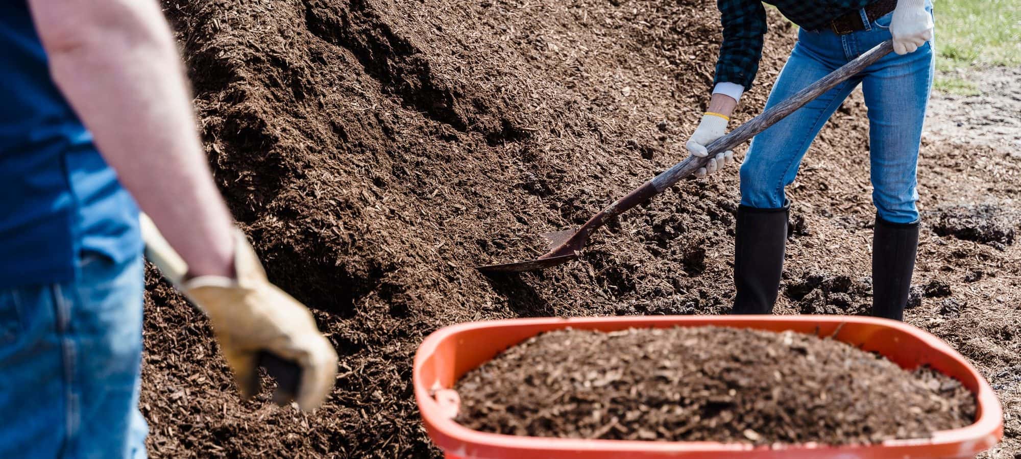 Two crew members moving soil with a wheelbarrow on a sunny job site