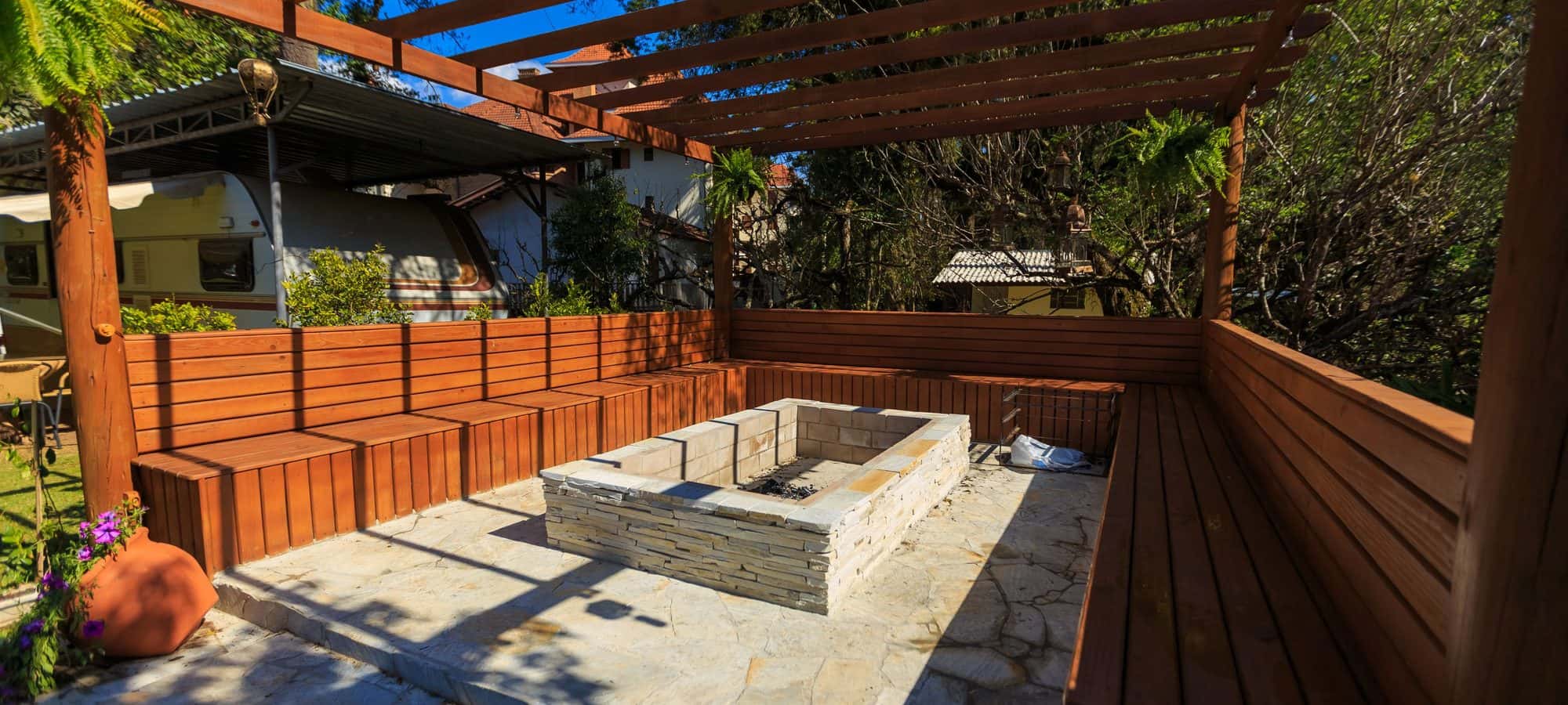 Stone fire pit surrounded by built-in wooden bench seating under a pergola